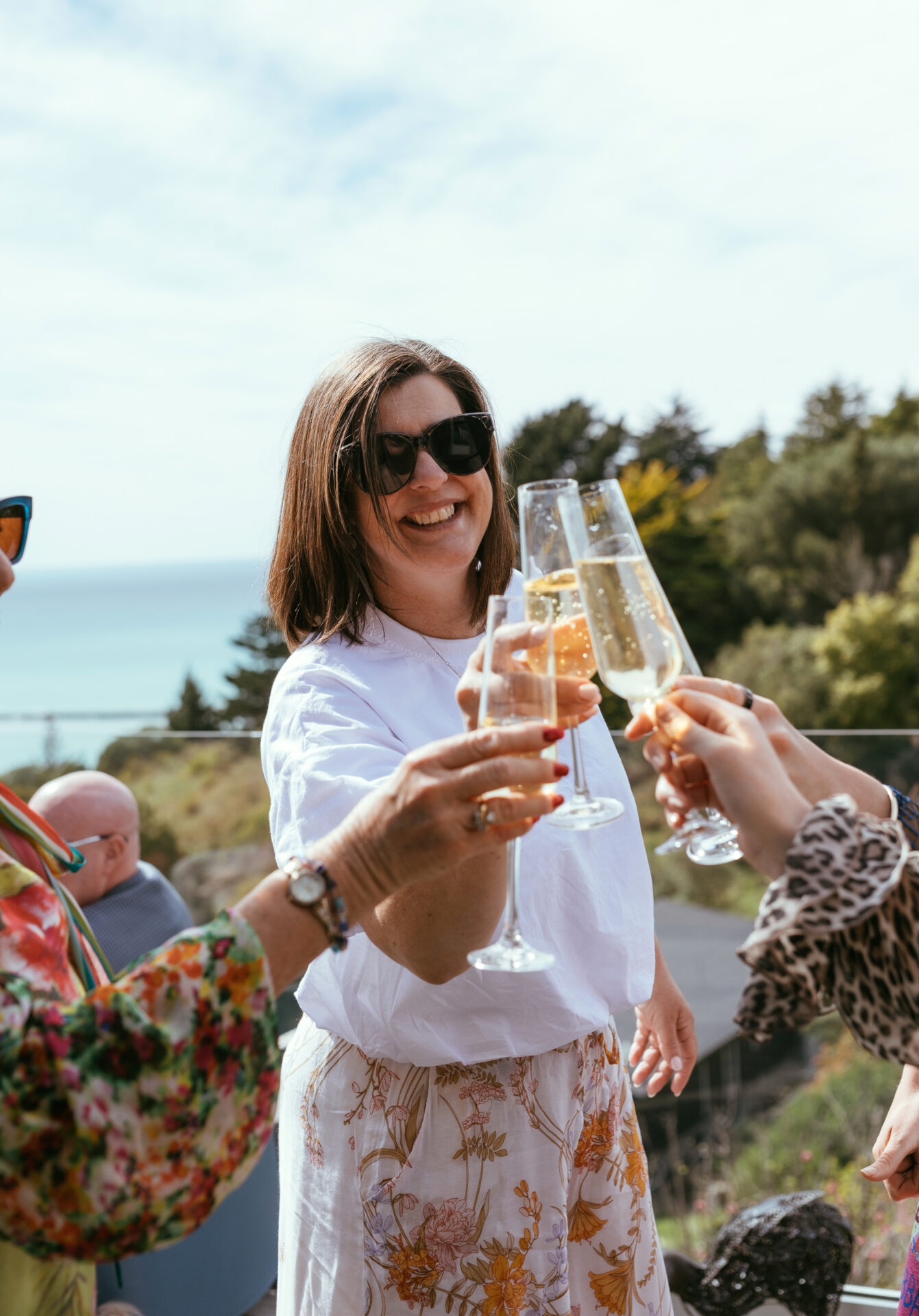 Women cheers 4 champagne glasses with a view of the ocean behind them
